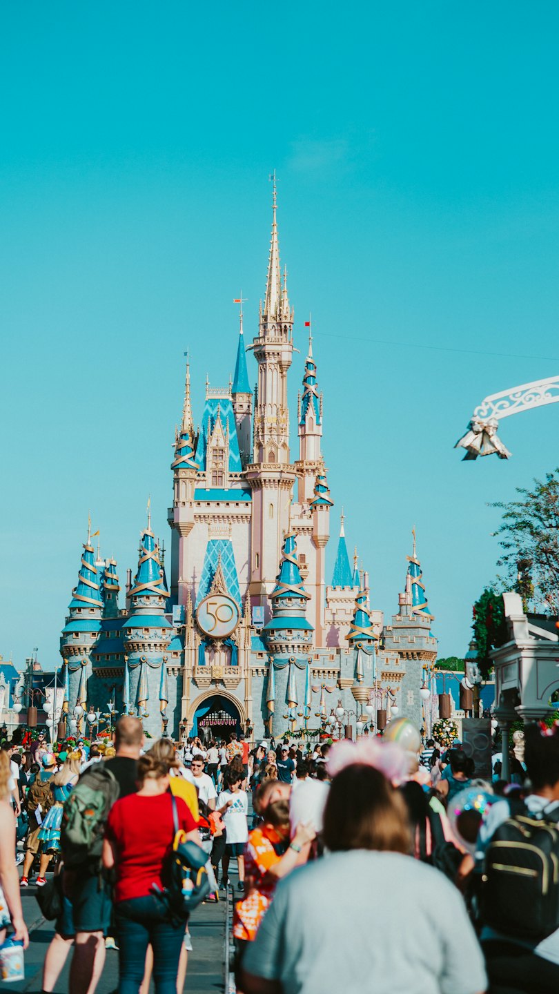 Crowds walking toward the decorated Cinderella Castle at a theme park.